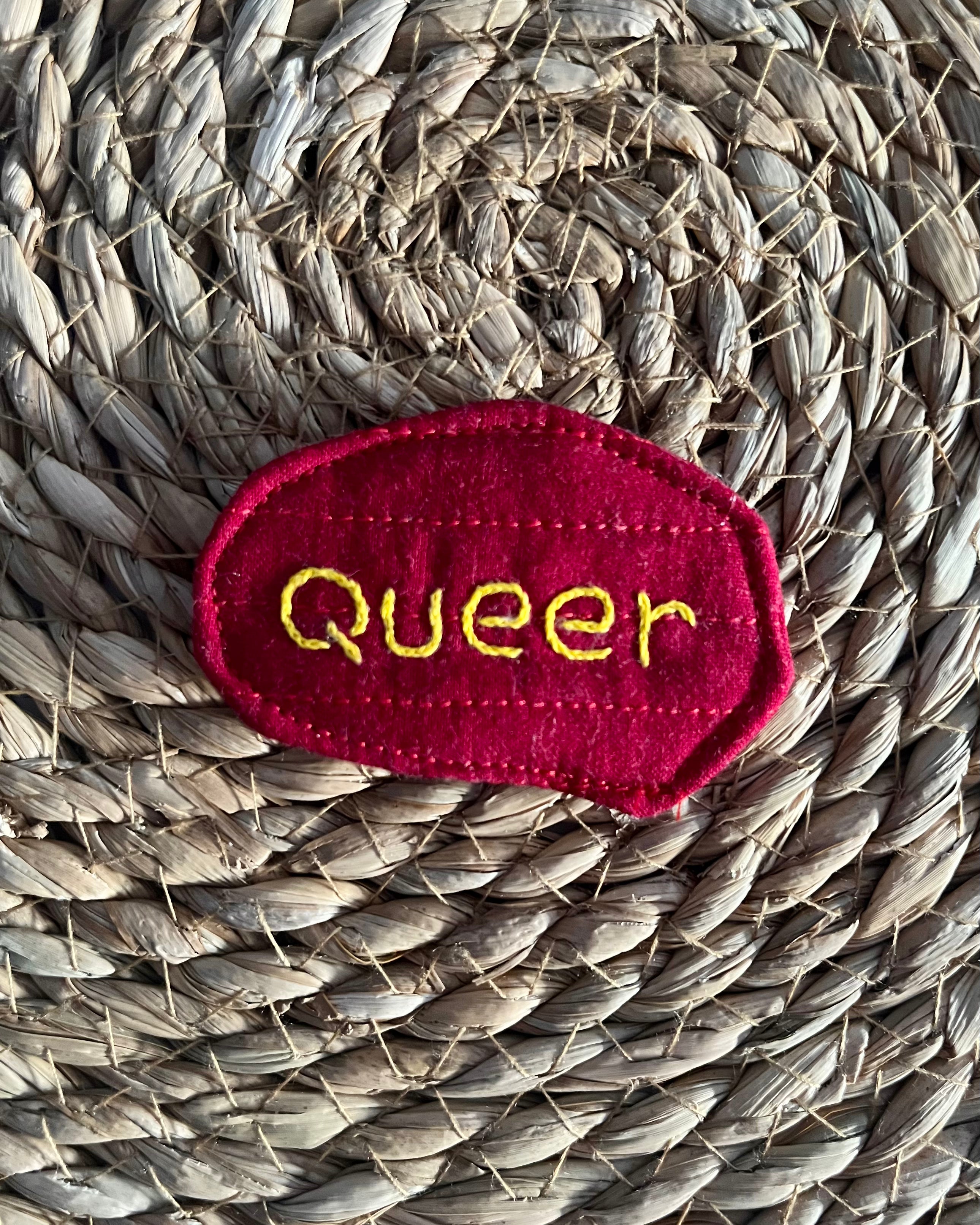 Hand-embroidered "queer" pin, quilted fabric offcut